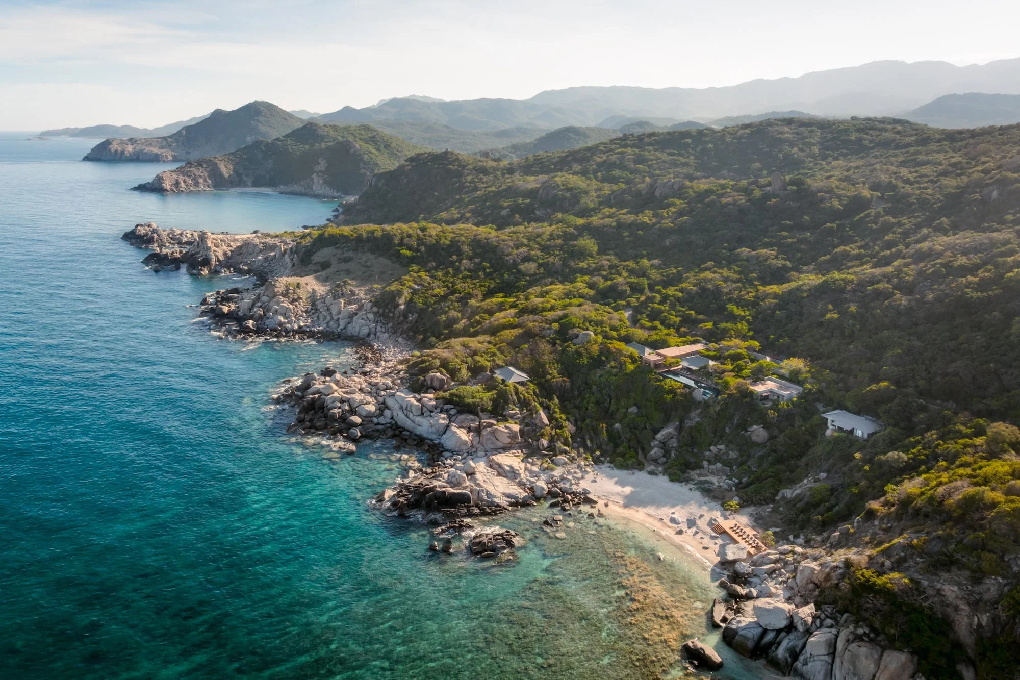  Aerial view of Amanoi Ocean Pool Residence, surrounded by lush forest and overlooking the ocean, with its infinity pool, pavilions and expansive outdoor terraces. 