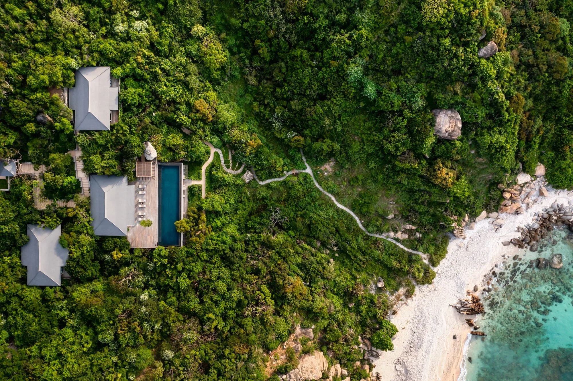  Aerial view of Amanoi Residence with living and dining pavilions and a large infinity swimming pool surrounded by expansive decking and a pathway down to the beach. 