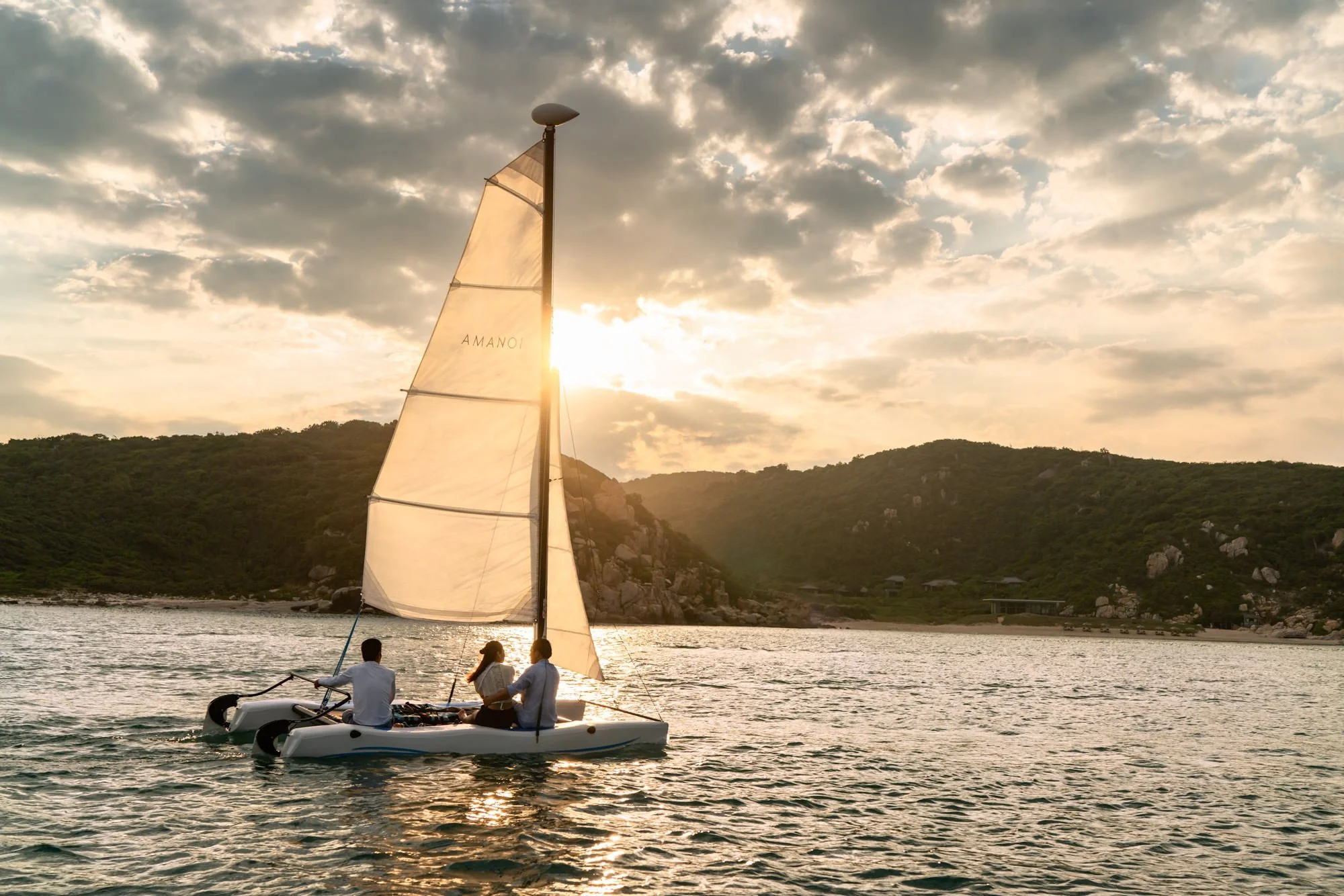  Amanoi sailing boat gliding through the bay at sunset, with guests enjoying the tranquil waters surrounded by lush, rocky coastline. 