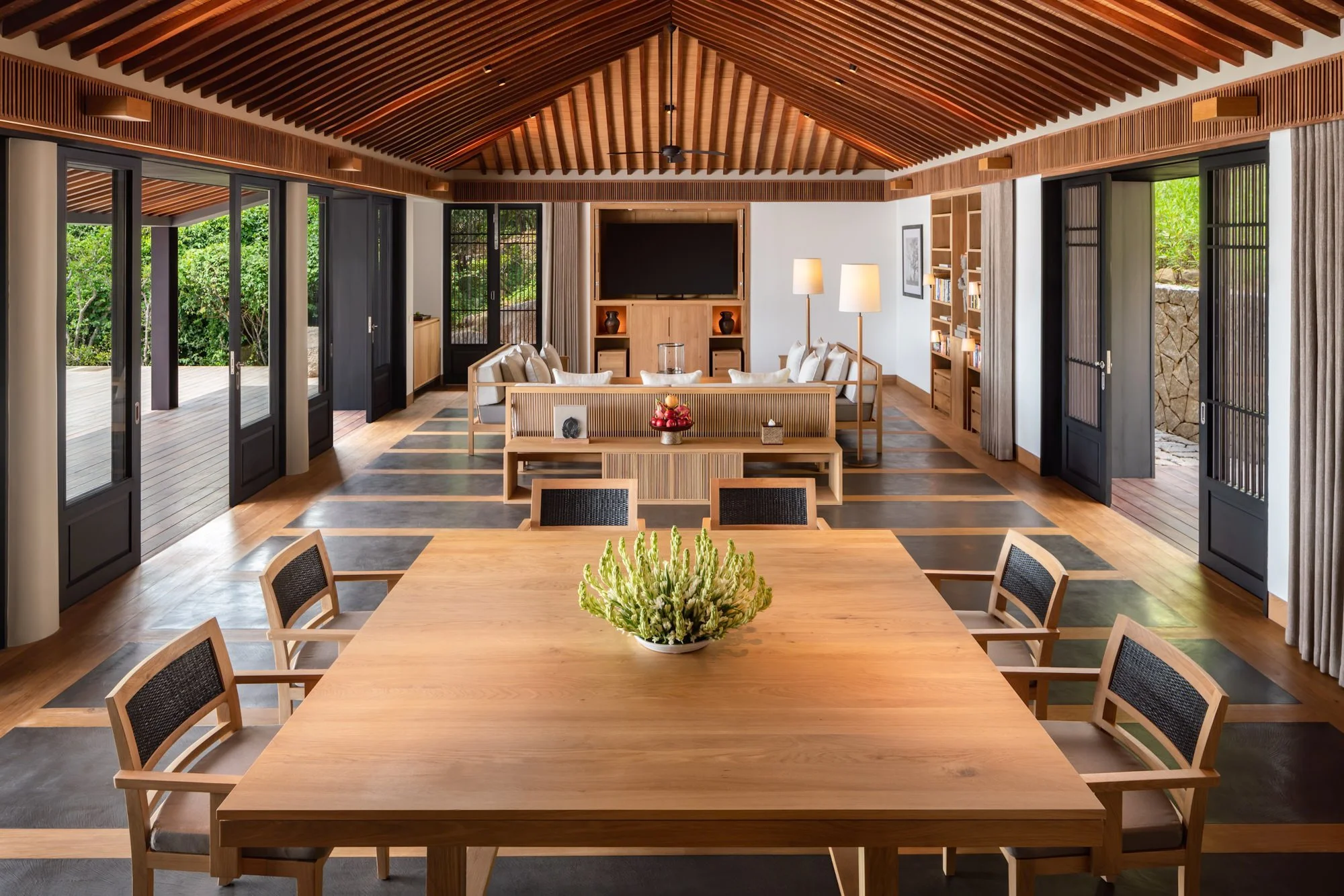  Amanoi Residence living pavilion with a large wooden dining table, lounge area and timber vaulted ceiling overlooking the surrounding forest. 