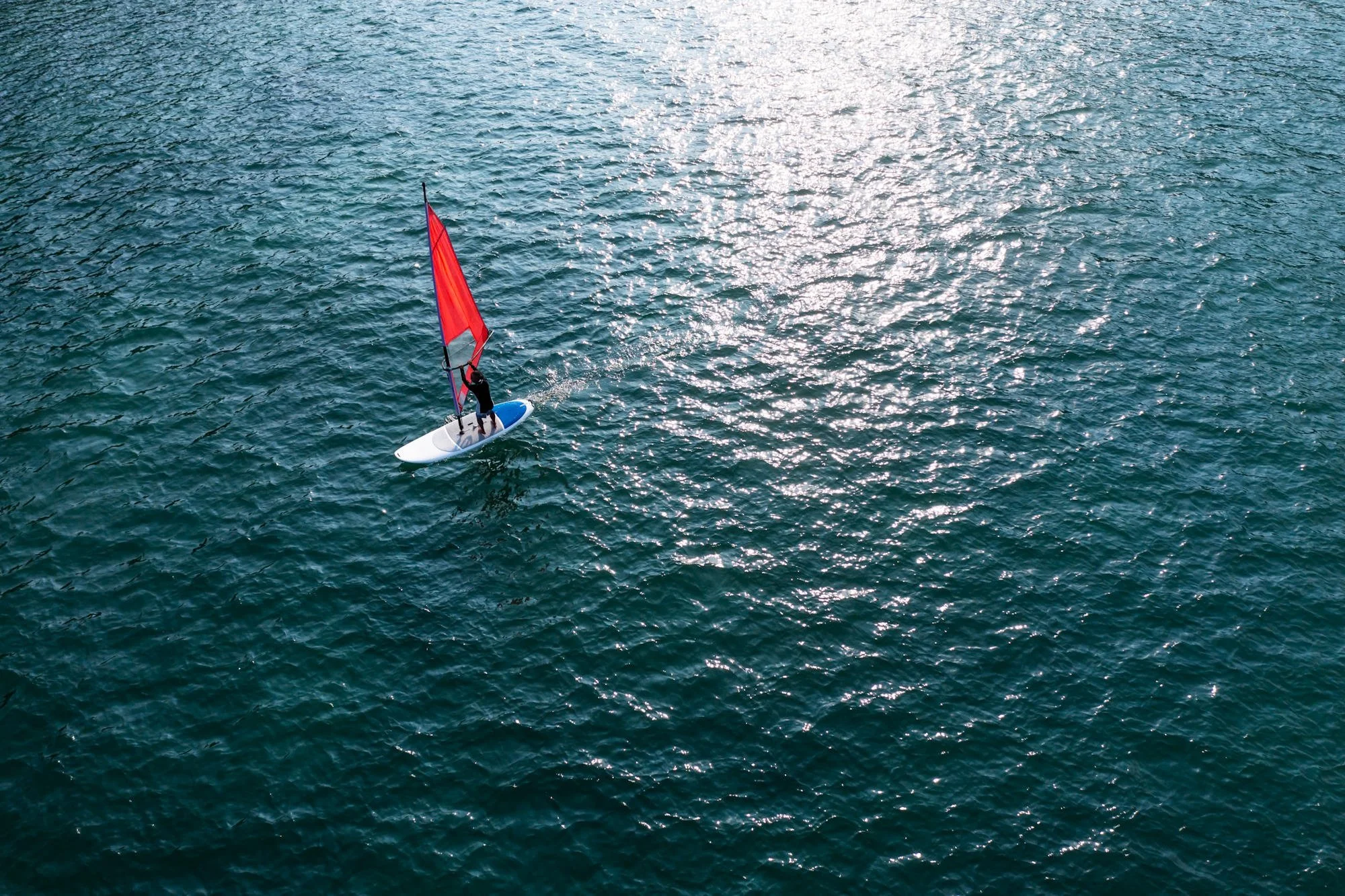 Amanoi guest wind surfing across the sunlit waters of Vinh Hy Bay on a red-sailed board. 