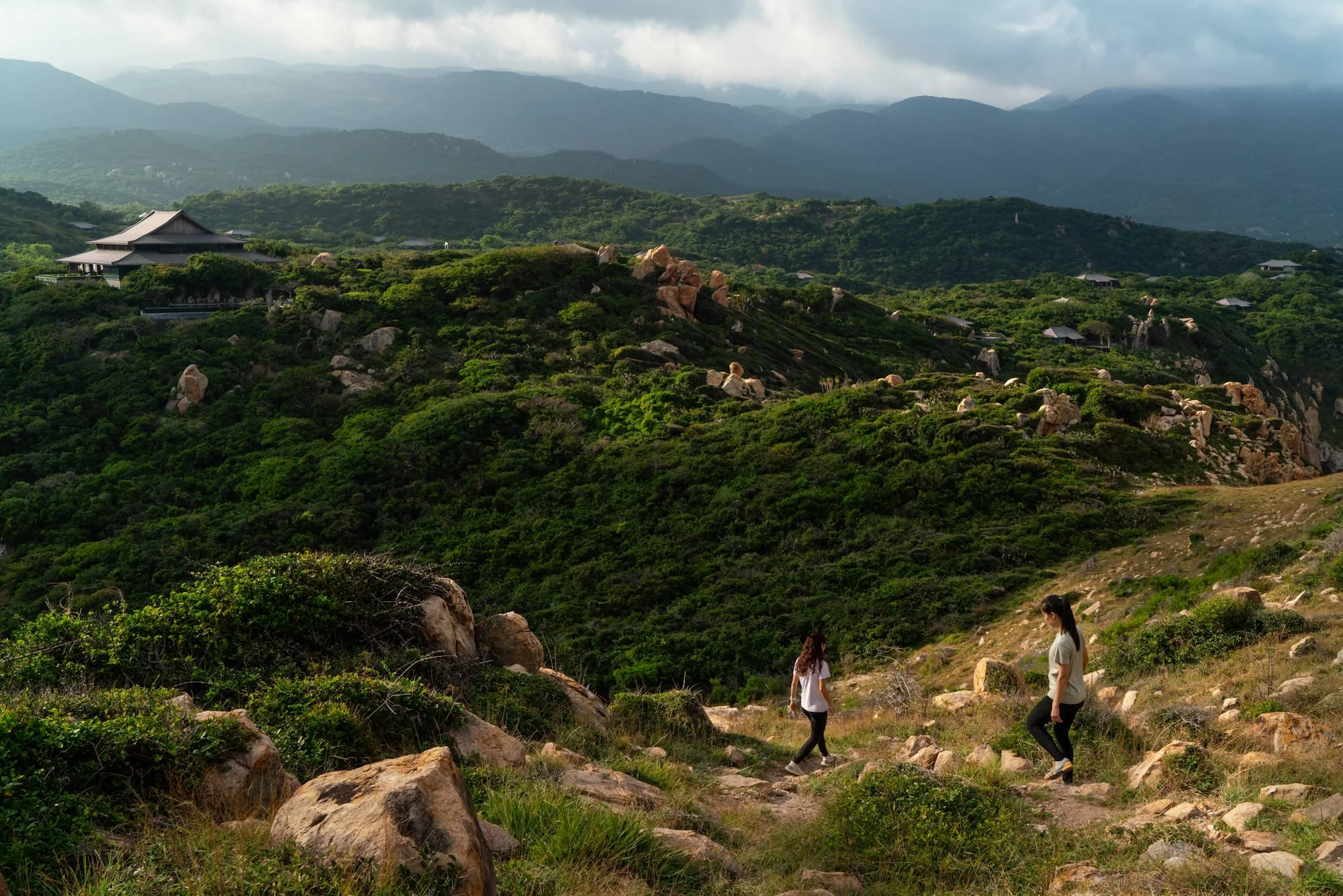  Guests hiking through the rugged landscape surrounding Amanoi, with lush vegetation, granite boulders and mountain views overlooking the resort. 