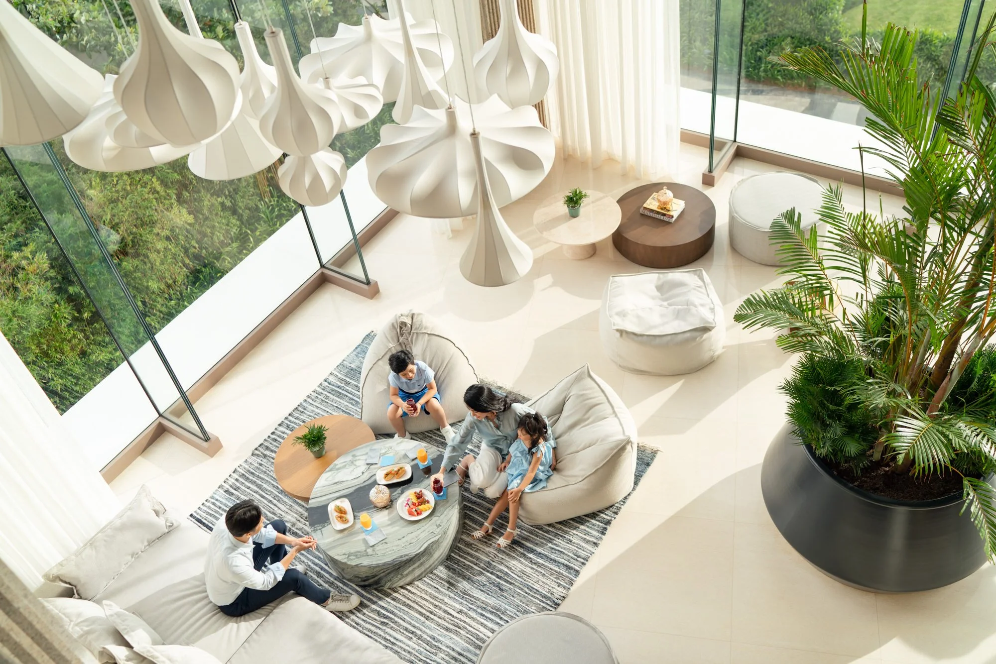  Quang Nam House Lounge & Bar at New World Hoiana Beach Resort, with a family relaxing in a light-filled lounge surrounded by floor-to-ceiling windows and tropical greenery. 