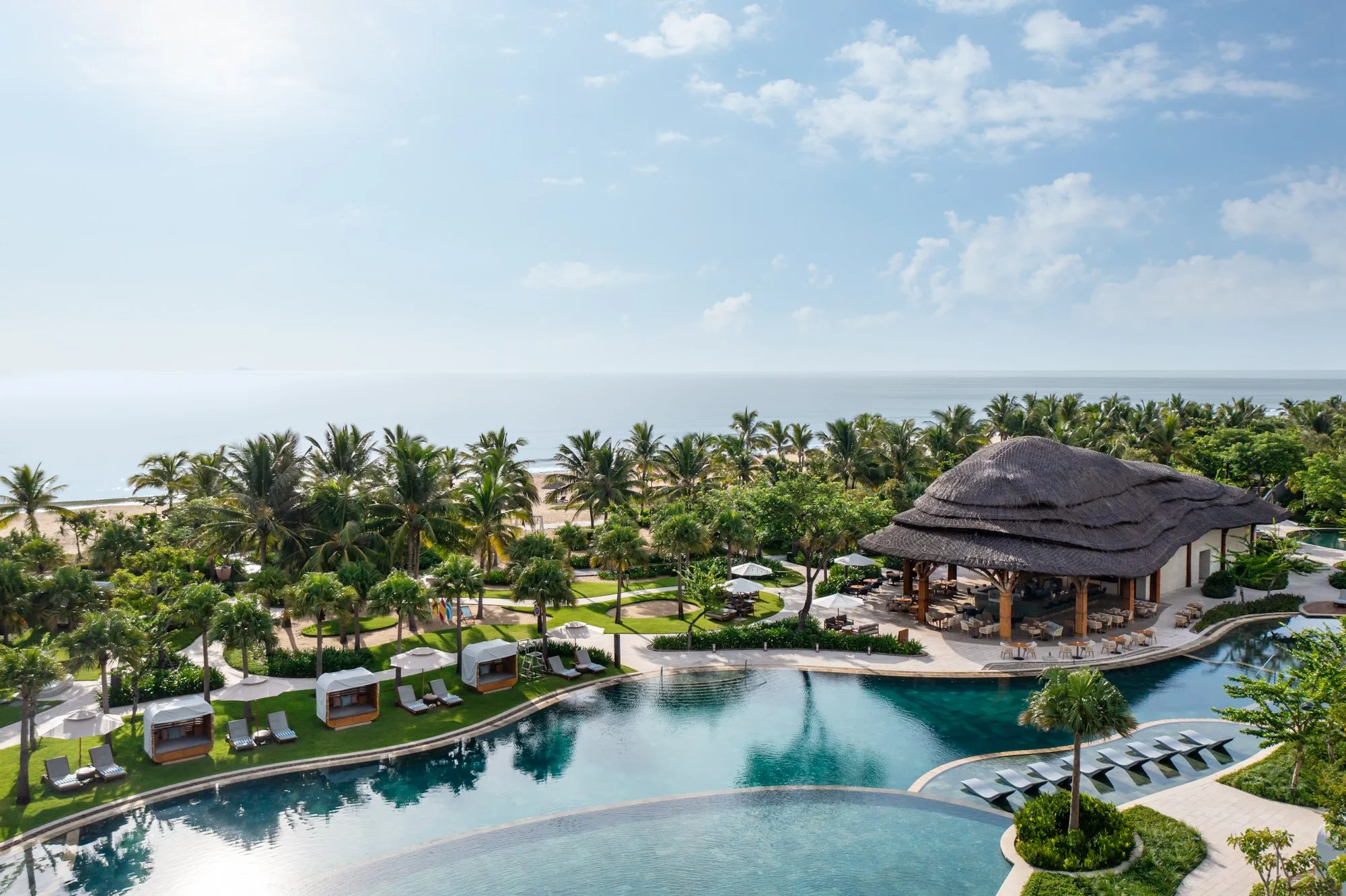  The thatched-roof Cove Restaurant pavilion overlooking Cove Pool, tropical gardens and the South China Sea at New World Hoiana Beach Resort. 
