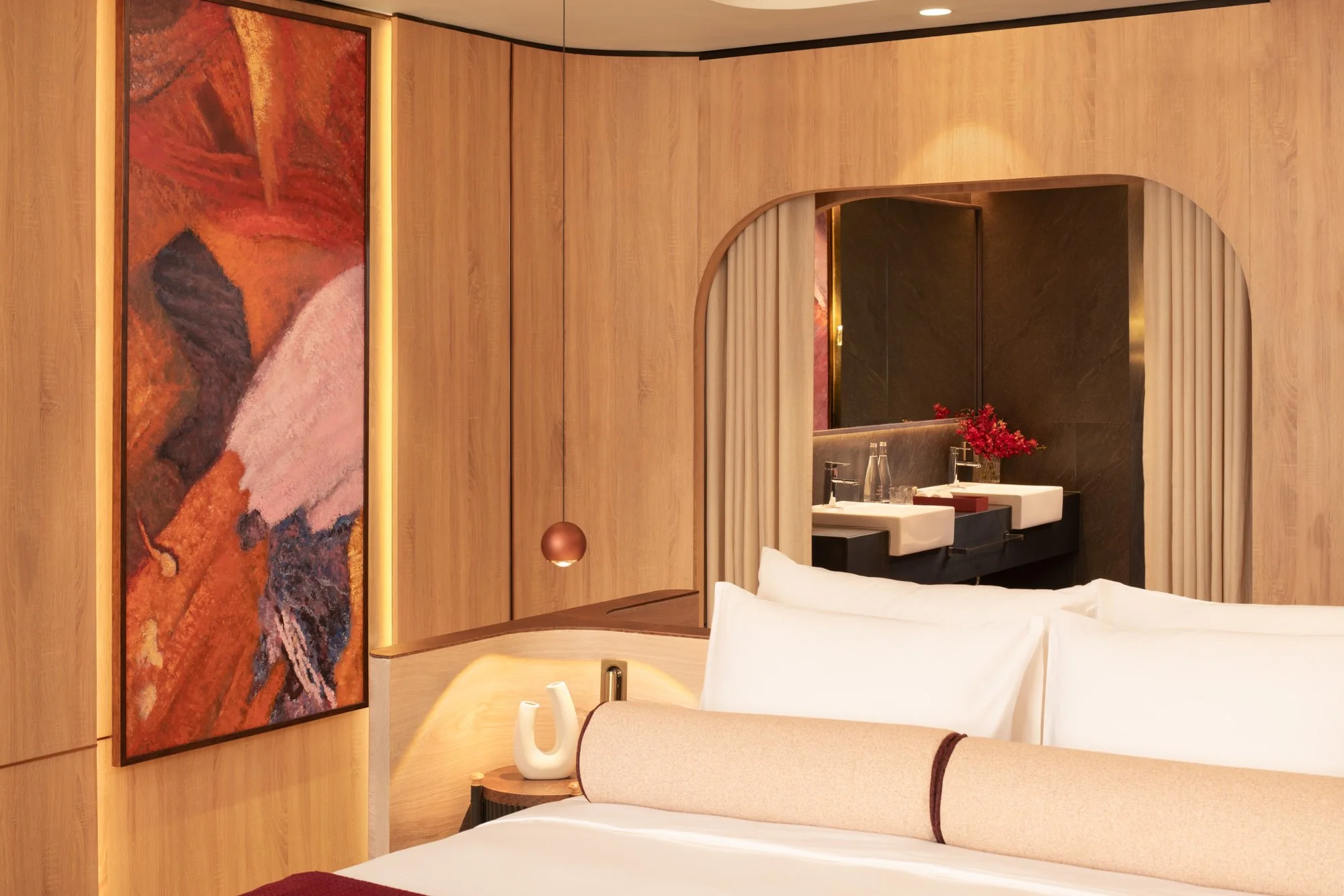  Reserve Suite Double at The Auberg Collection Hotel, featuring a king bed, curved oak-panelled walls, abstract artwork and an arched opening to the vanity area. 