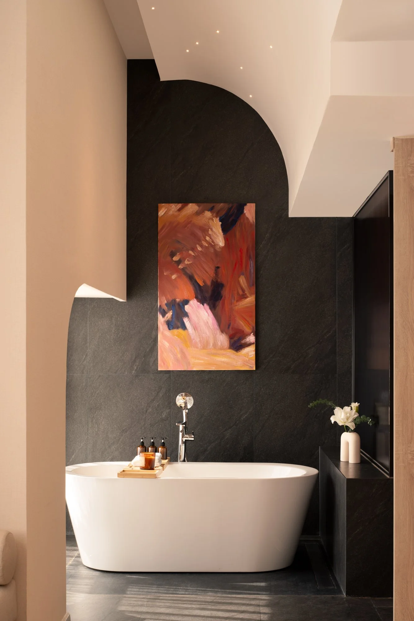  Modern bathroom in the Signature Suite Double at The Auberg Collection Hotel, featuring a white freestanding bathtub beneath a colourful abstract artwork set against a curved wall, creating a calm and elegant retreat. 