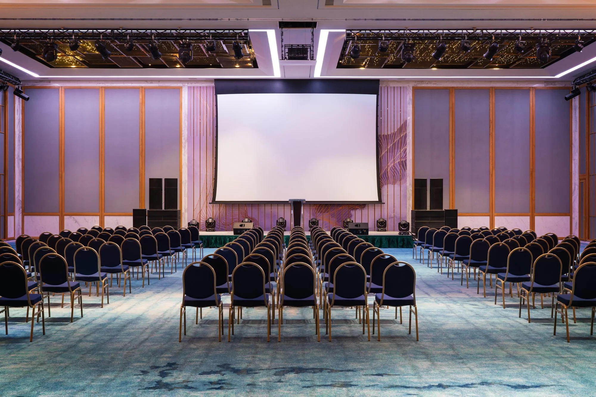  Brightly lit Zurich Ballroom at Mövenpick Resort Cam Ranh, with rows of chairs facing a large projection screen, set up for a conference, presentation or formal event. 