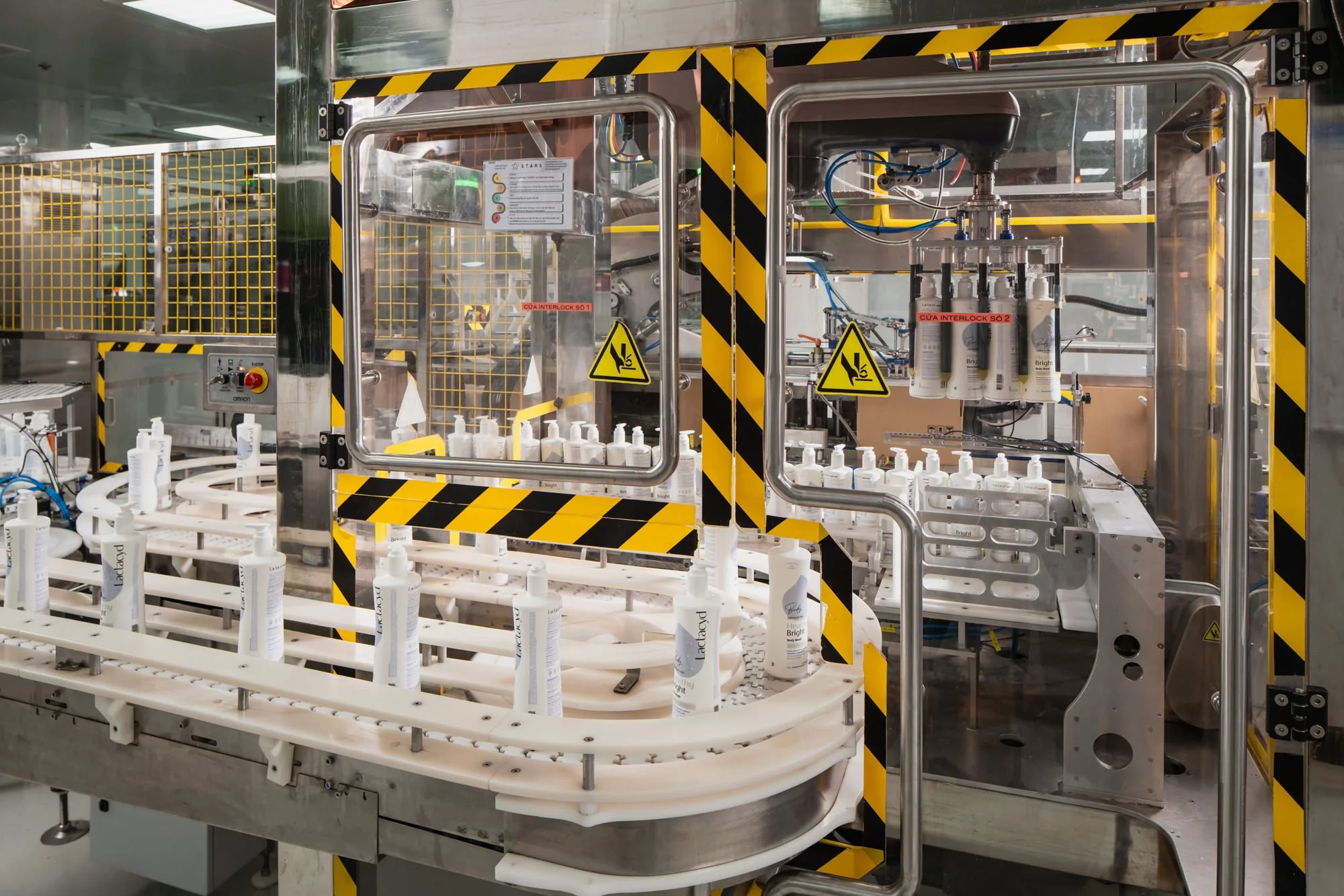  An automated packaging line moves white Lactacyd bottles through stainless-steel machinery behind glass safety panels at the Opella manufacturing facility in Ho Chi Minh City, Vietnam. 