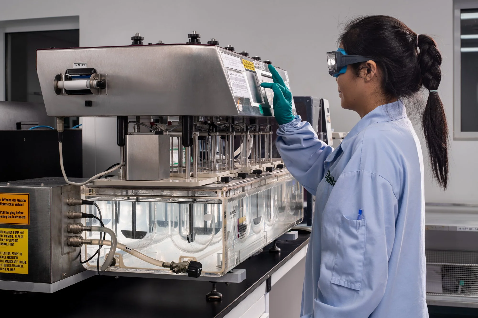  A lab technician in protective glasses and gloves adjusts a stainless-steel scientific instrument in a bright laboratory at the Opella manufacturing facility in Ho Chi Minh City, Vietnam. 