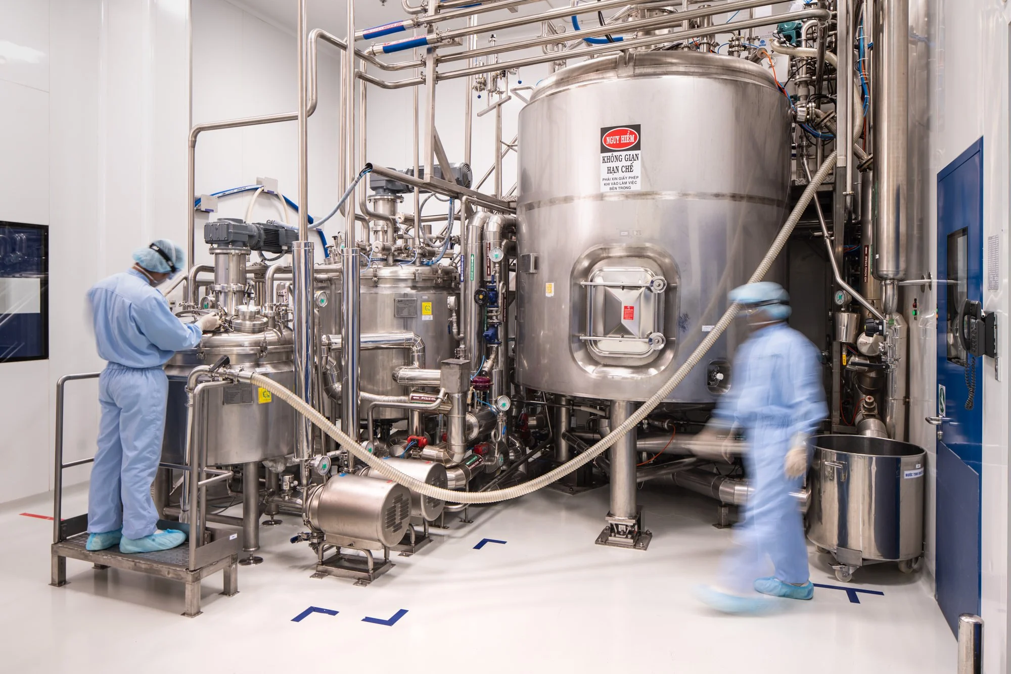  Two workers in blue protective suits operate stainless-steel tanks and pipes in the Liquid Pharma Workshop at the Opella manufacturing facility in Ho Chi Minh City, Vietnam. 