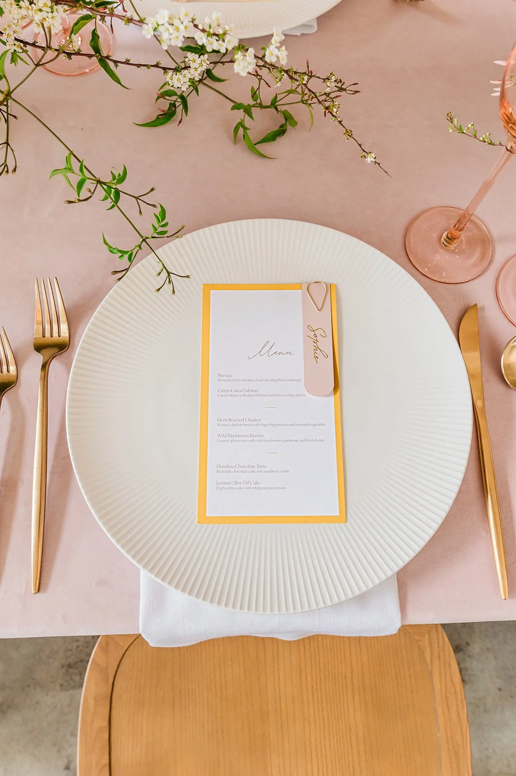 Spring brunch place setting detail — Magnolia Marks menu card, gold flatware, cherry blossom branches