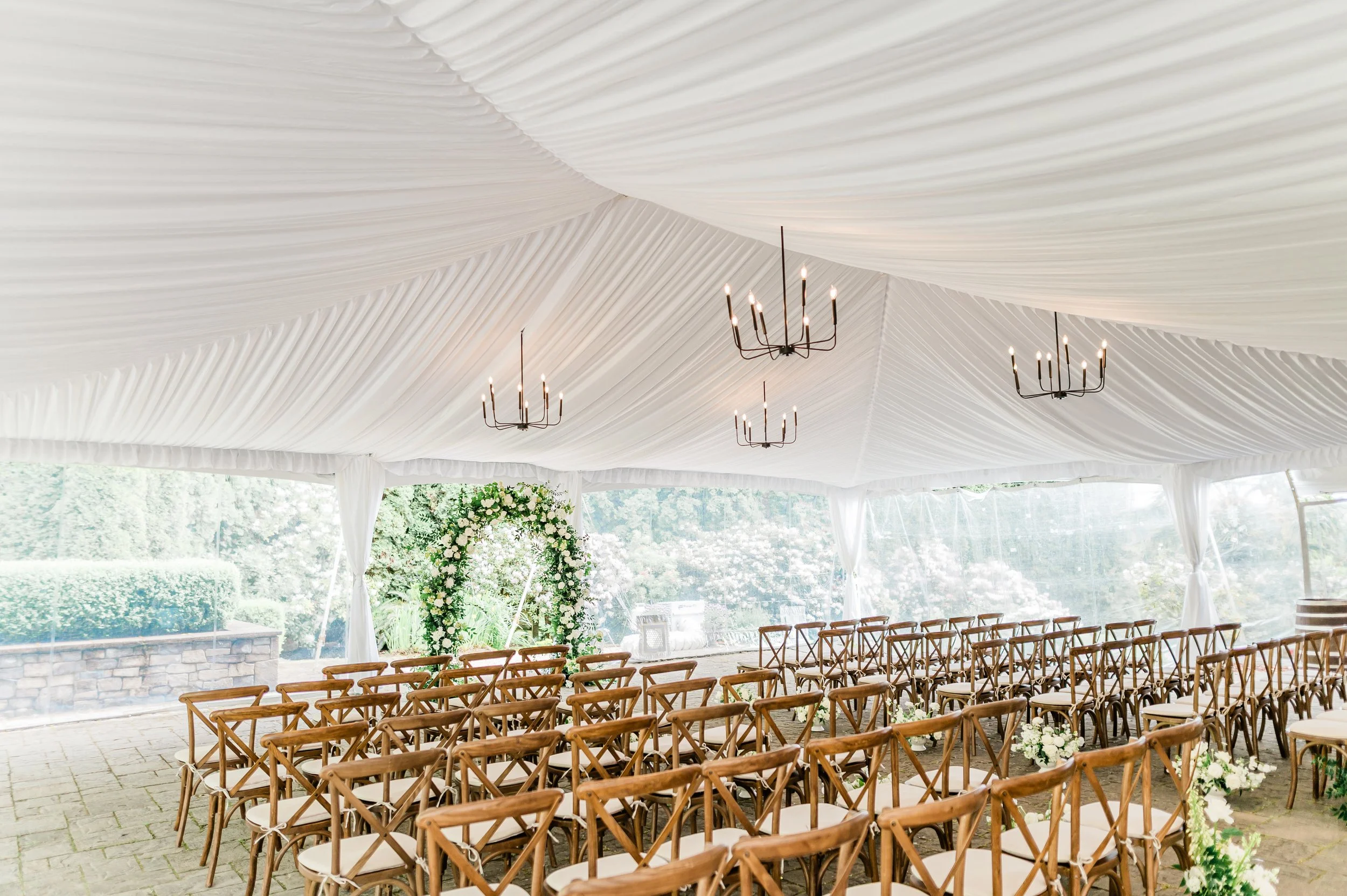 Indoor Wedding reception at chateau Lill.  rows of wooden chairs arranged under a white draped tent ceiling, decorated with elegant chandeliers and floral arrangements in the background.