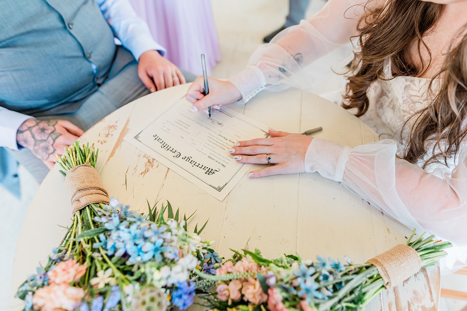 Newlyweds signing their marriage license beside a wildflower bouquet