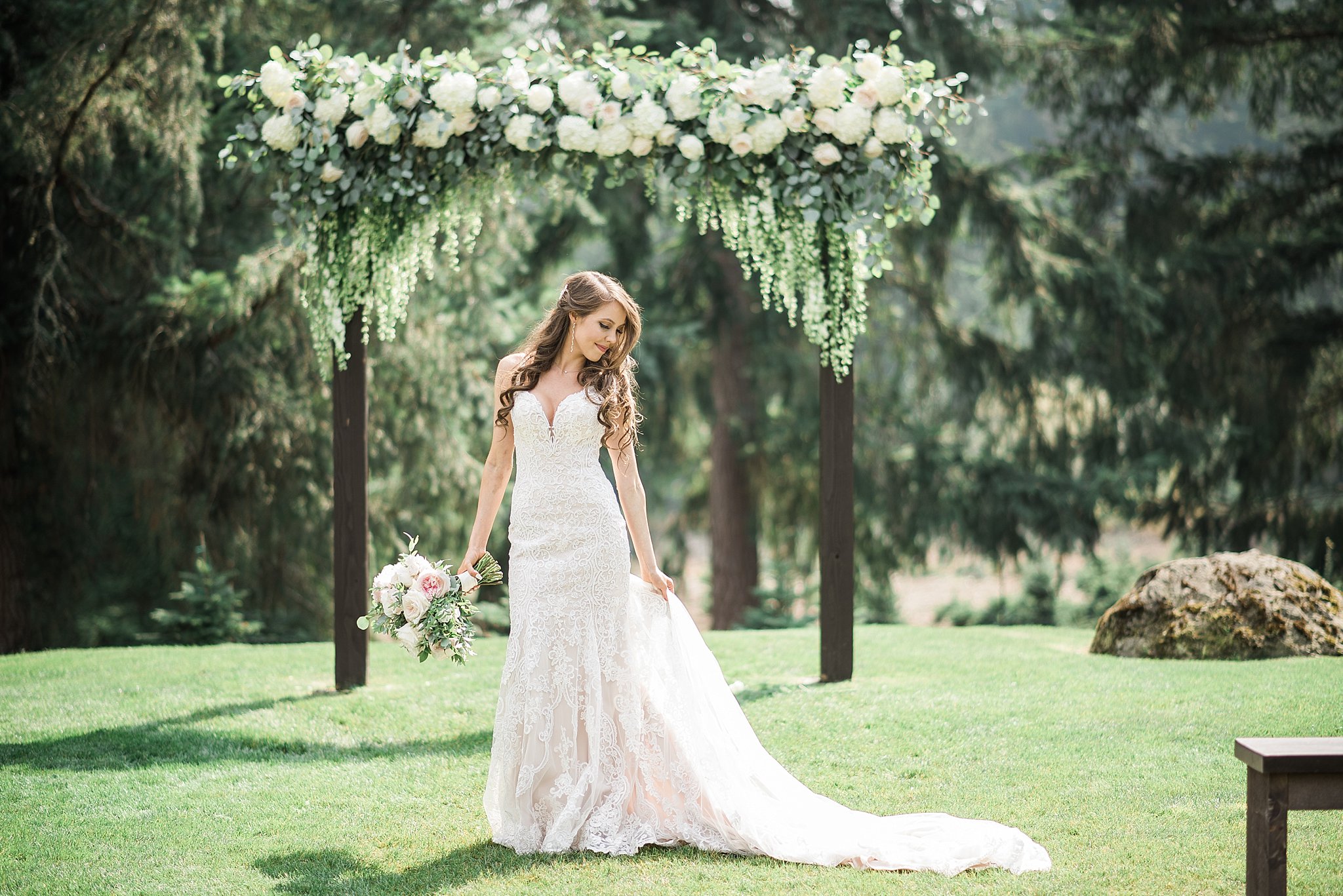 The bride in front a gorgeous white & green floral arch by Bloom