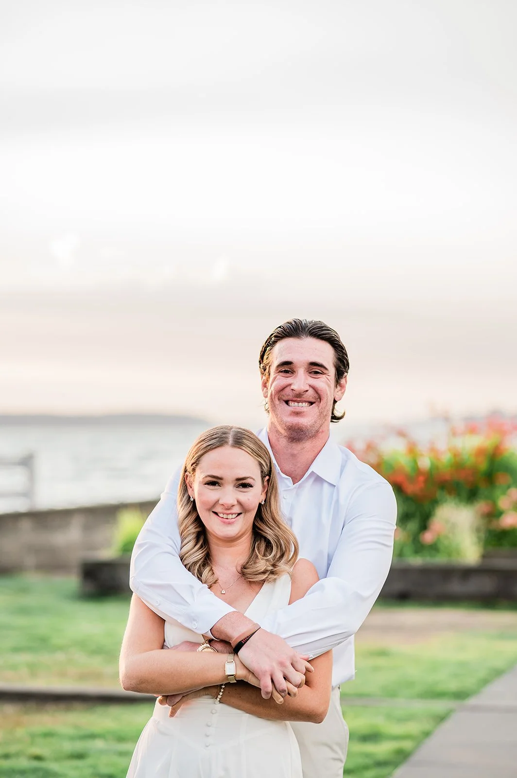 Fiancé hugging fiancée from behind, both laughing, at Mukilteo Lighthouse Park