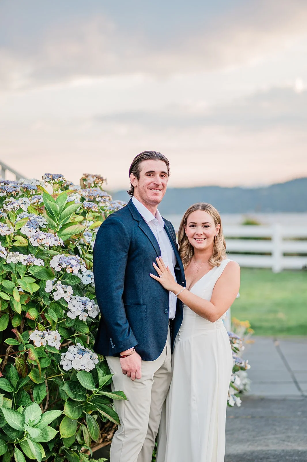 Couple smiling in front of hydrangeas with Puget Sound behind them