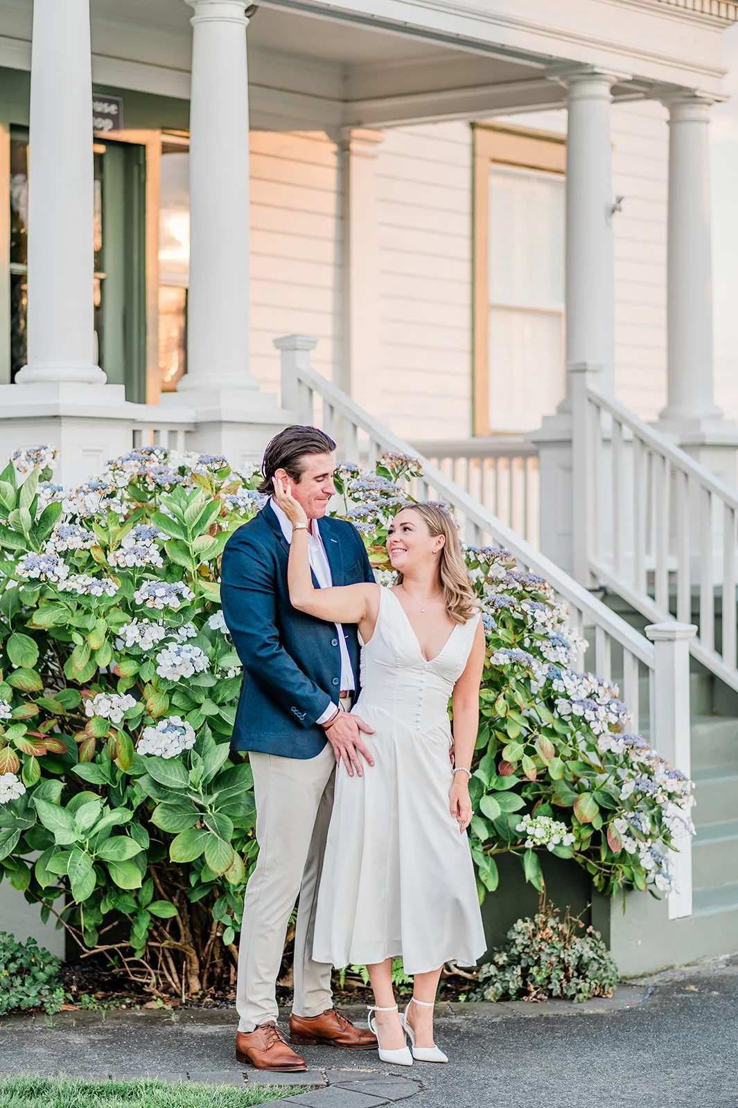 Couple on the white porch steps of the Mukilteo lighthouse keeper's house with hydrangeas