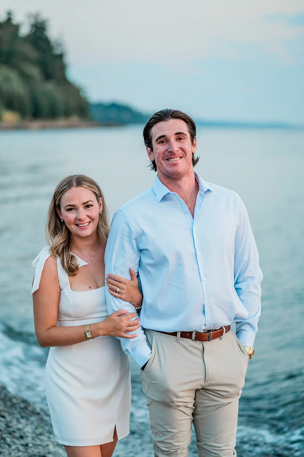 Engaged couple standing arm in arm at the water's edge in Mukilteo