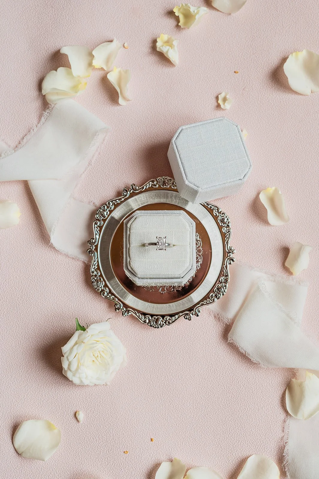 Wedding rings in a white octagonal ring box on a silver tray with rose petals