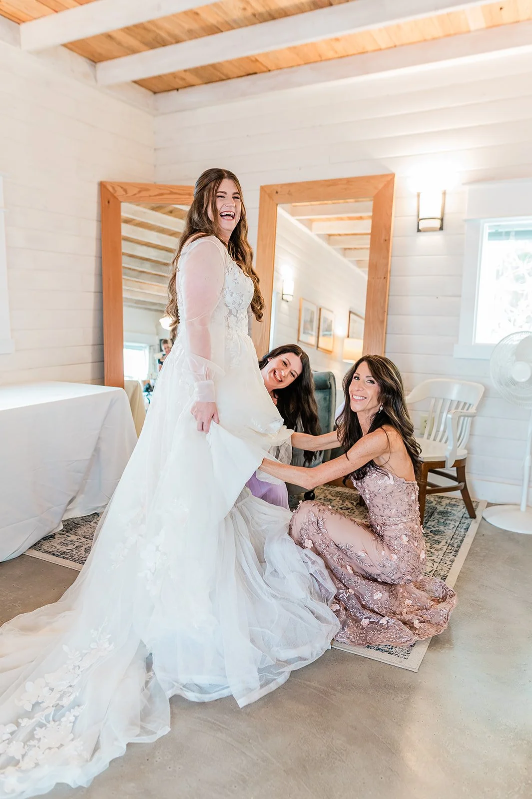 Mother of the bride adjusting her daughter's wedding gown in the bright white bridal cottage