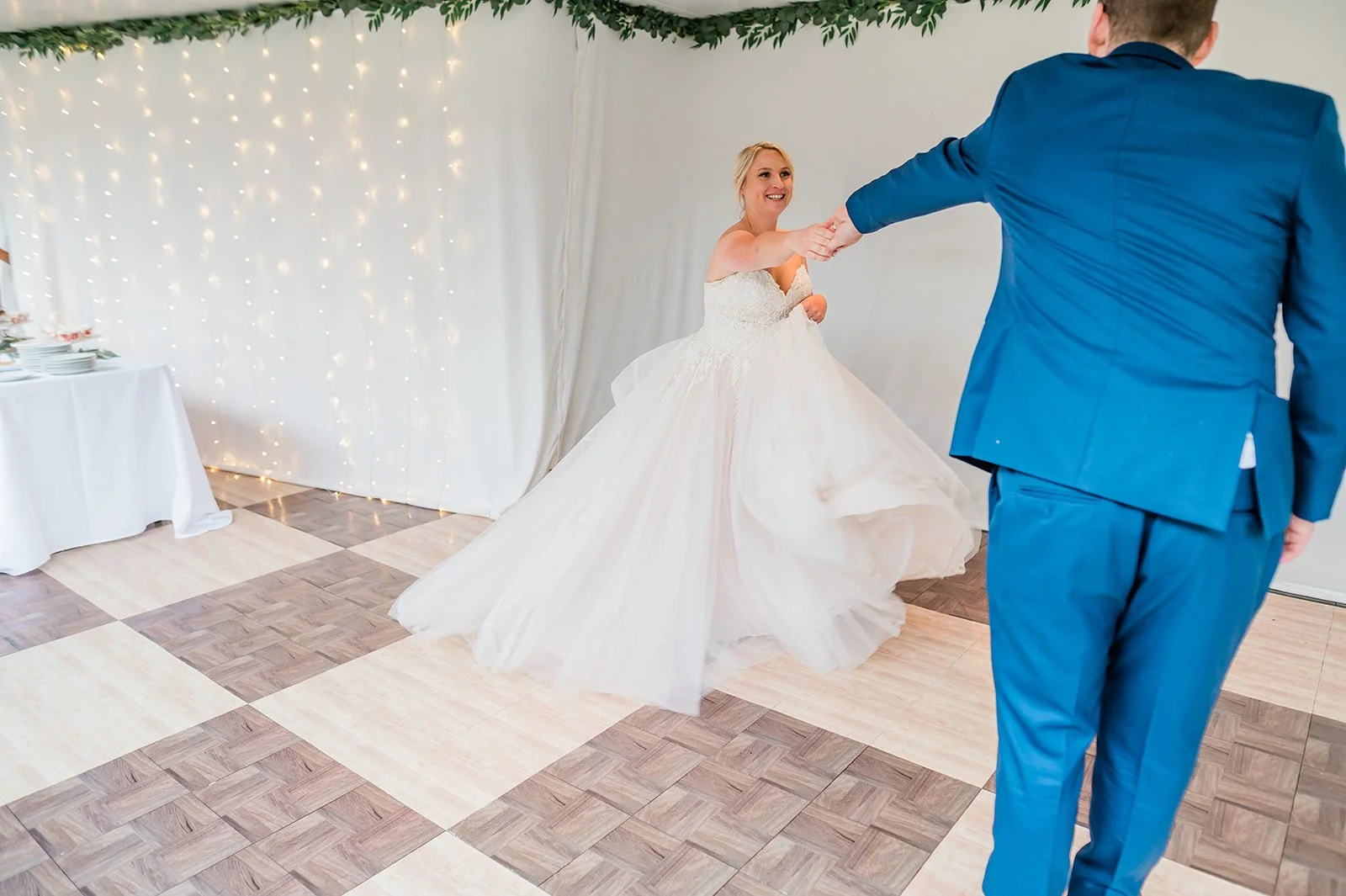 Groom in a blue suit twirling his bride on the checkered dance floor at The Carey Gardens