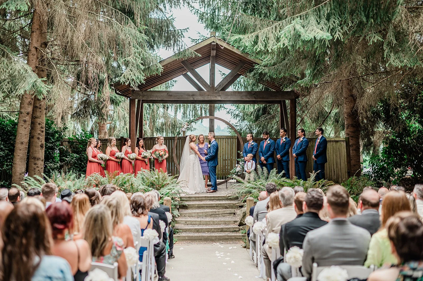 Wide view of a forest wedding ceremony under the wooden arbor at Woodland Meadow Farms in Snohomish