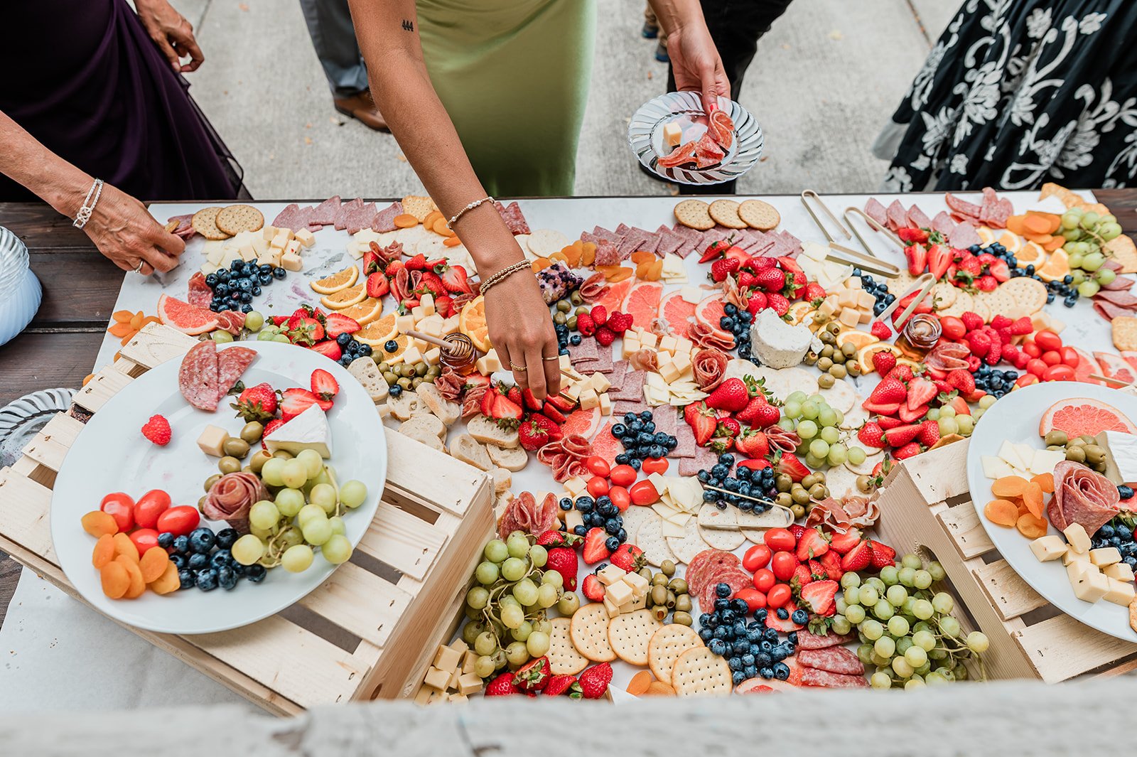 Guests reaching for fruit and cheese from a colorful grazing board at cocktail hour
