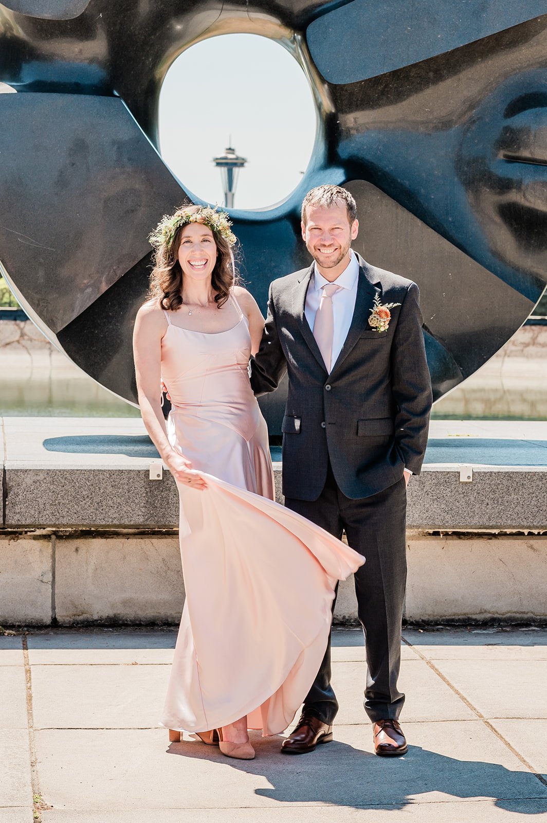 Bride and groom smiling in front of the Black Sun sculpture with Space Needle view, Volunteer Park Seattle