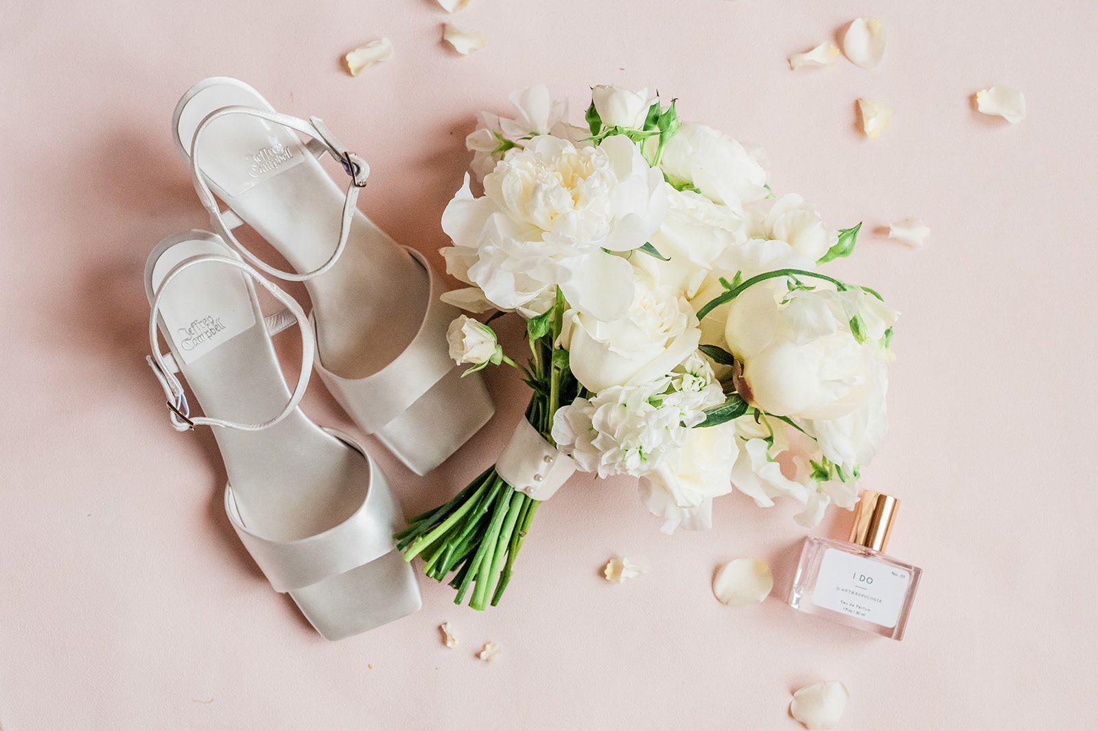 Bridal sandals, white peony bouquet and perfume styled on blush with rose petals