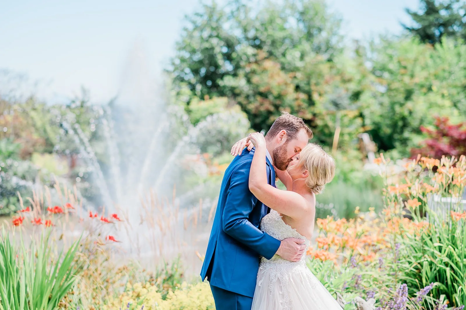Bride and groom embracing among orange florals with the garden fountain spraying behind them