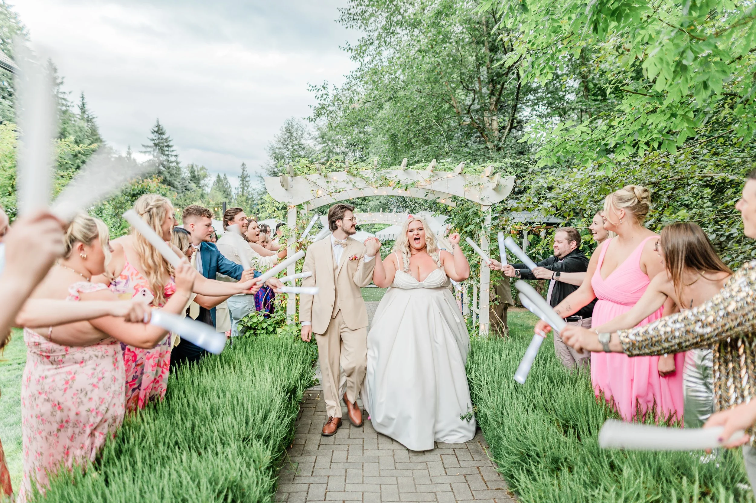 Bride and groom walking through a floral arch as guests cheer with confetti streamers at their Jackson Manor wedding