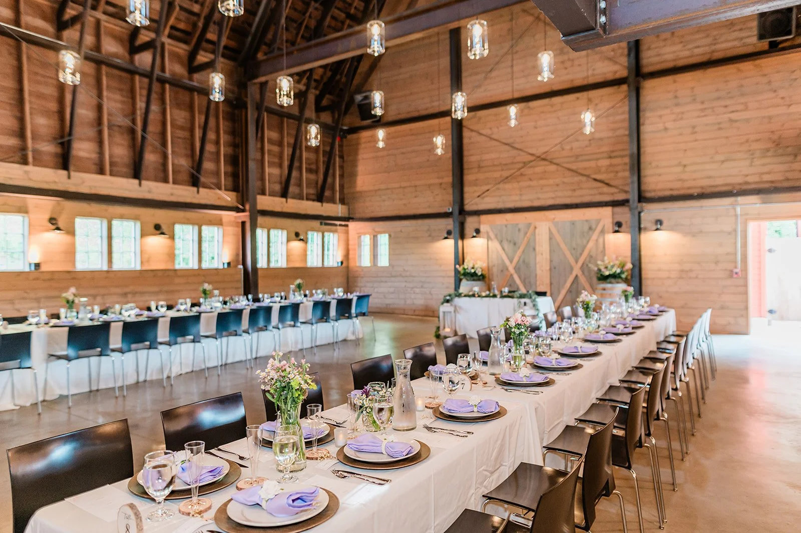 Long family-style reception tables with lavender napkins inside the barn at Marionfield Farm