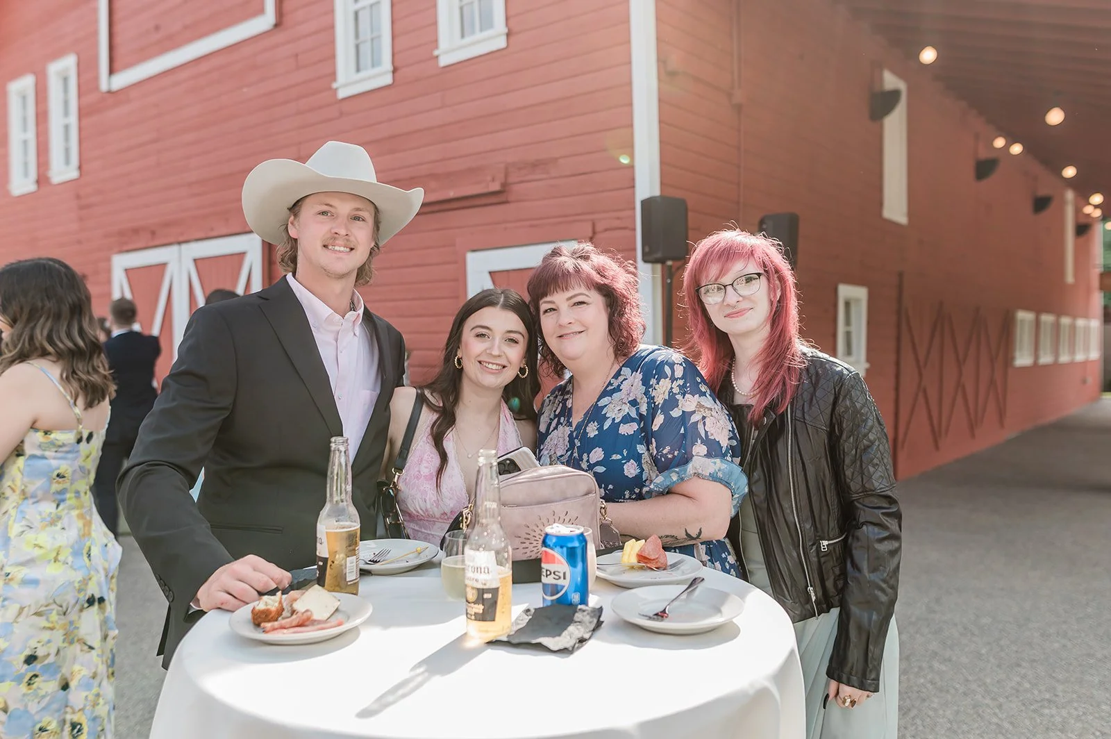 Wedding guests laughing at a cocktail table beside the red barn at Marionfield Farm