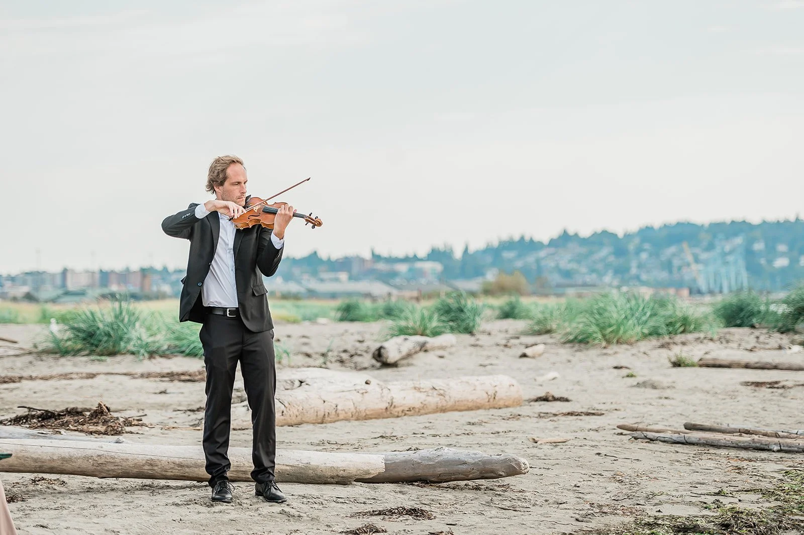 Violinist performing during outdoor beach wedding ceremony on Jetty Island Everett Washington surrounded by driftwood and sea grass