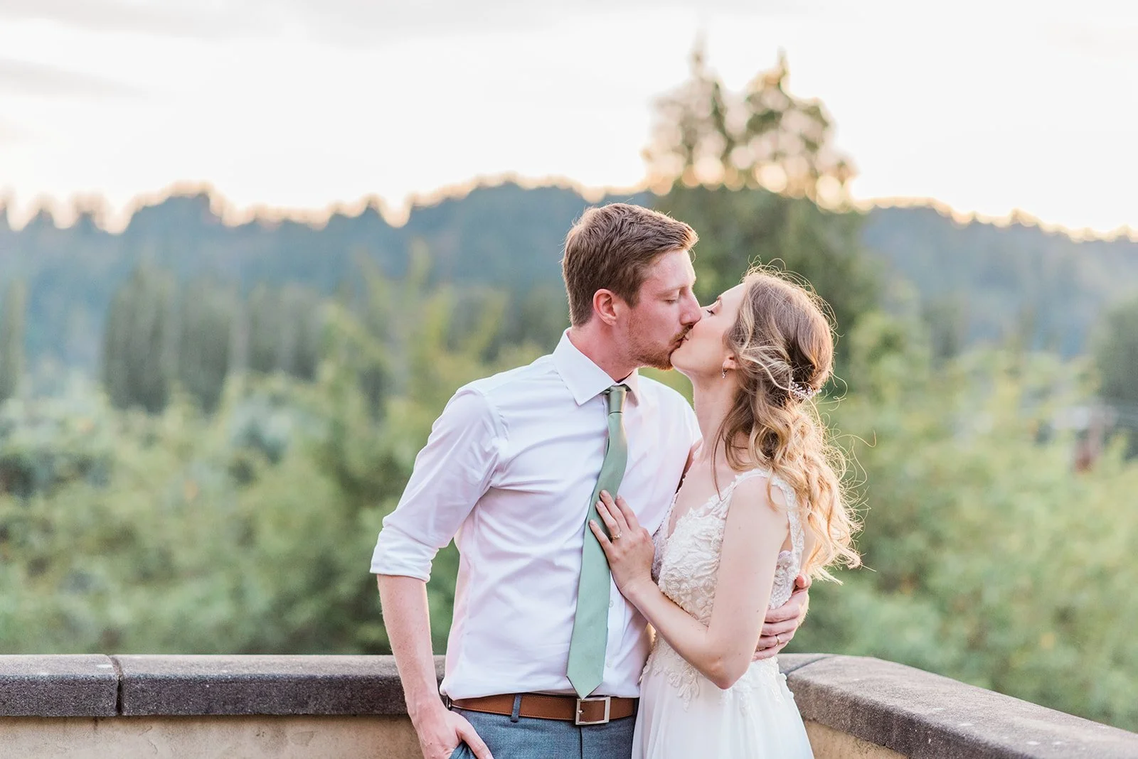 Groom lifting bride in front of the entry portico at Lairmont Manor, wisteria climbing the white stucco wall and the ornate oval window above them