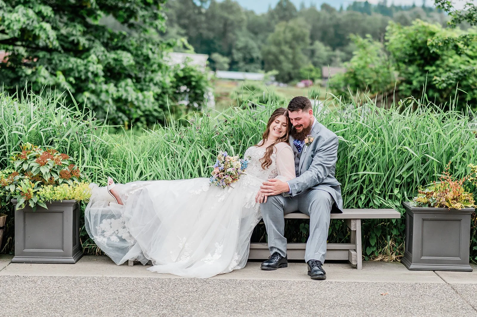 Bride and groom relaxing together on a garden bench surrounded by tall grasses at Marionfield Farm