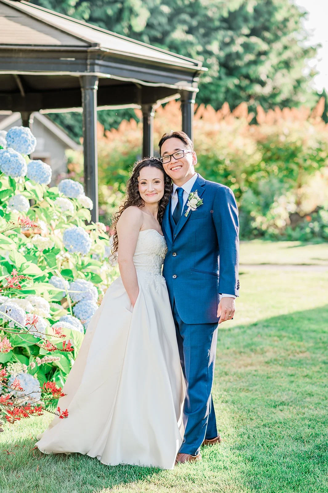 Bride and groom smiling beside tall blue hydrangeas in a Snohomish summer garden