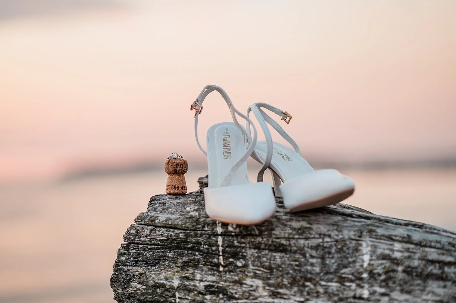 White heels and champagne cork on driftwood at sunset