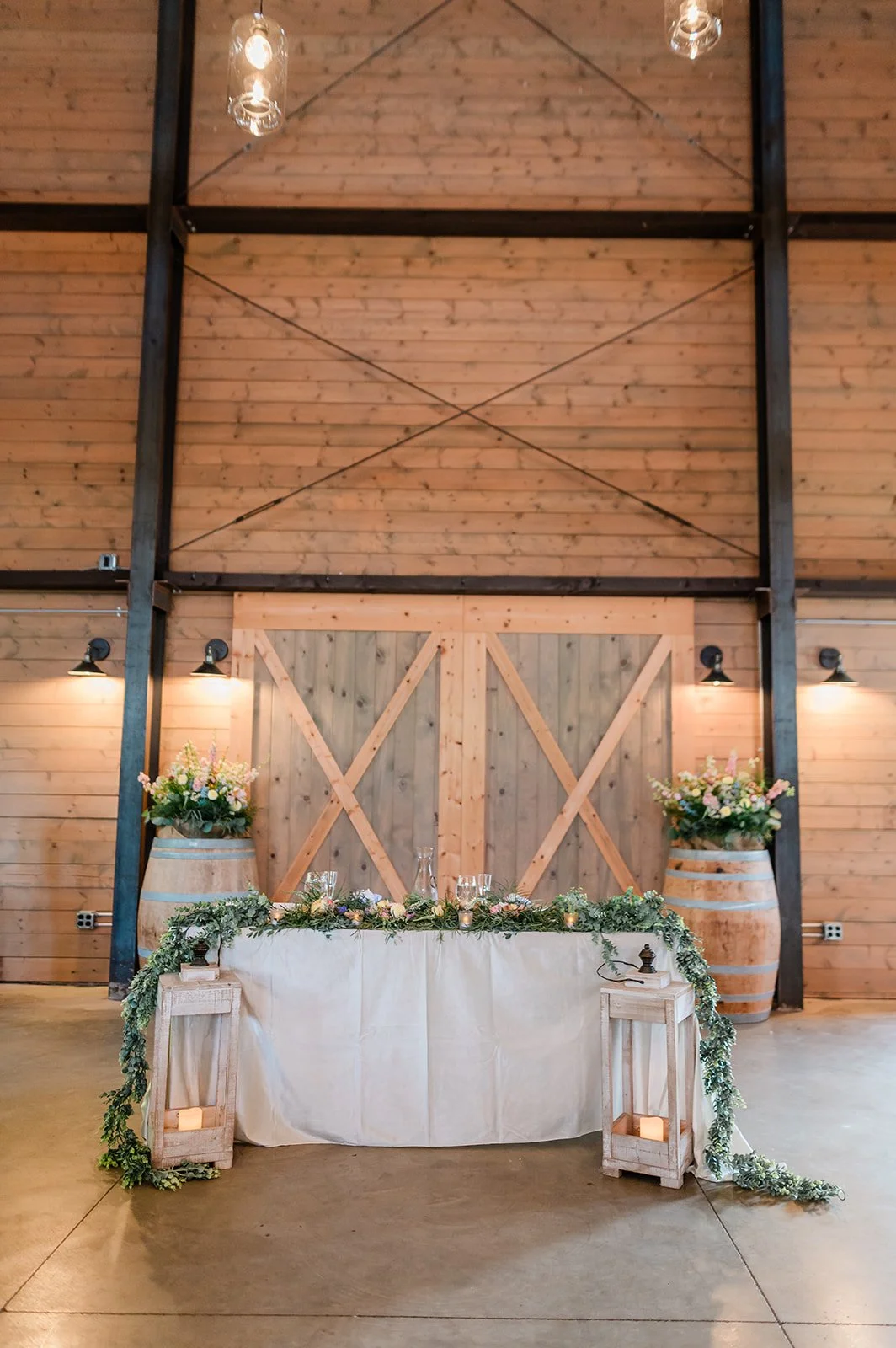 Sweetheart table with greenery garland in front of rustic X-braced barn doors