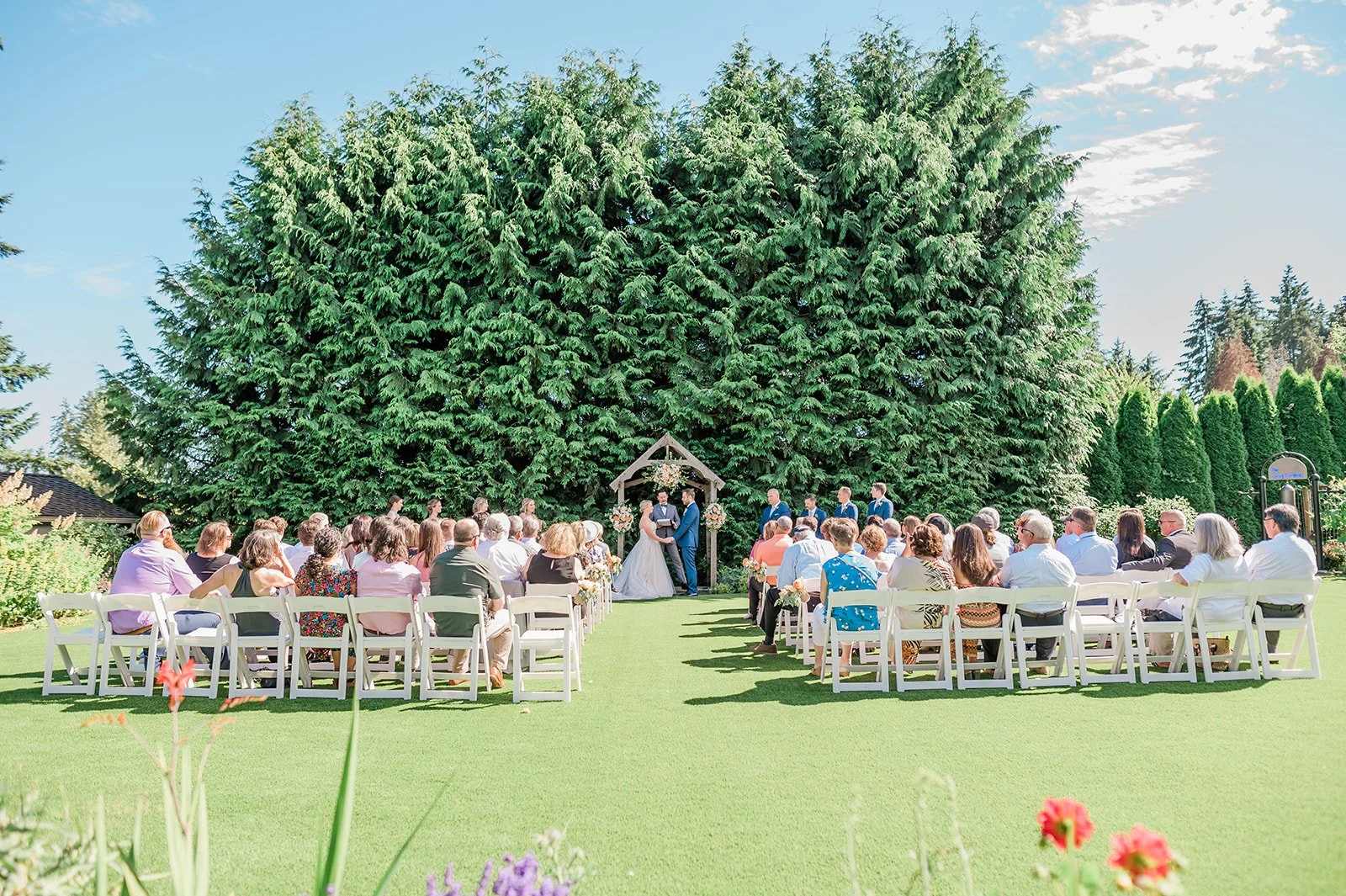 Outdoor wedding ceremony on the shaded upper lawn at The Carey Gardens surrounded by tall evergreens