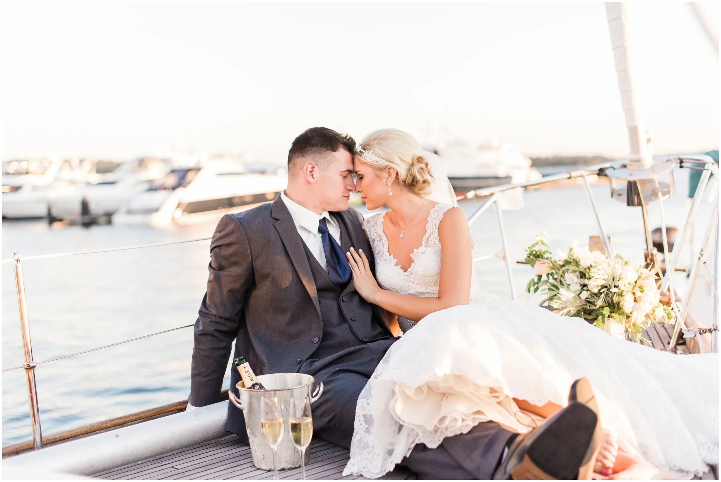 A newlywed couple sitting close on a seattle sailboat boat dock, with water and boats in the background, celebrating their wedding with champagne and flowers.