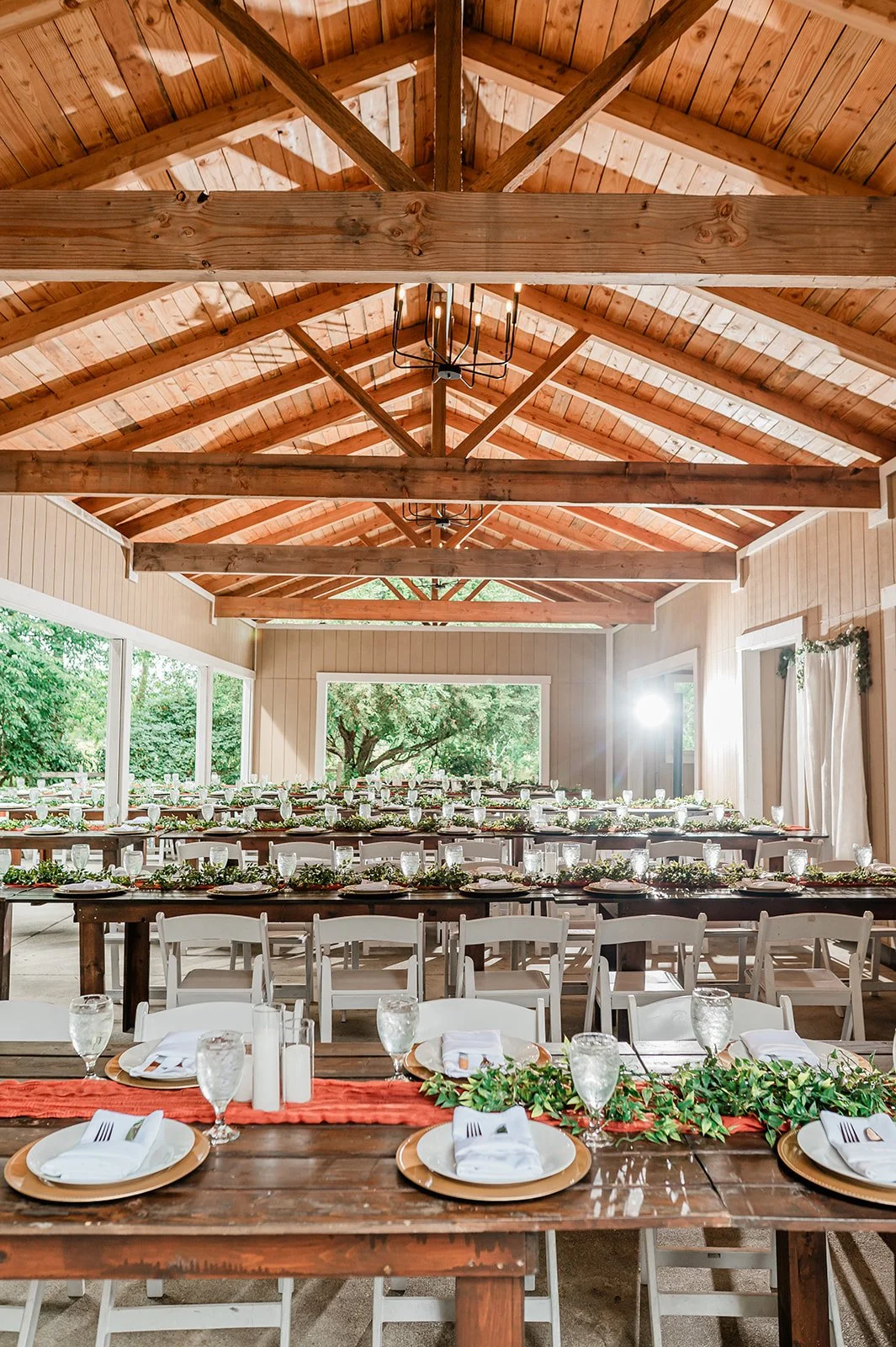 Covered reception pavilion with chandeliers and long wooden tables set for a wedding
