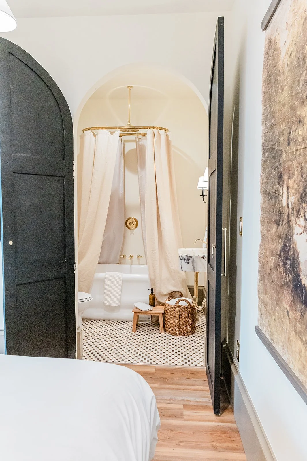 908 luxury suite bathroom — soaking tub cocooned in linen canopy drapes, brass curtain rod, original tile floor
