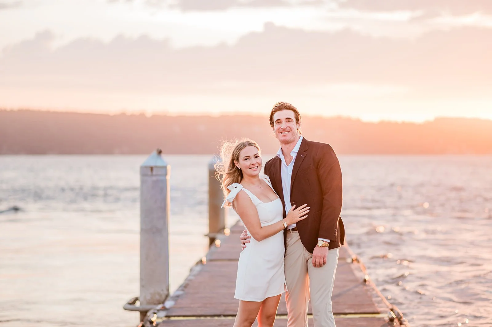 Wide sunset photo of an engaged couple on the dock over the water in Mukilteo