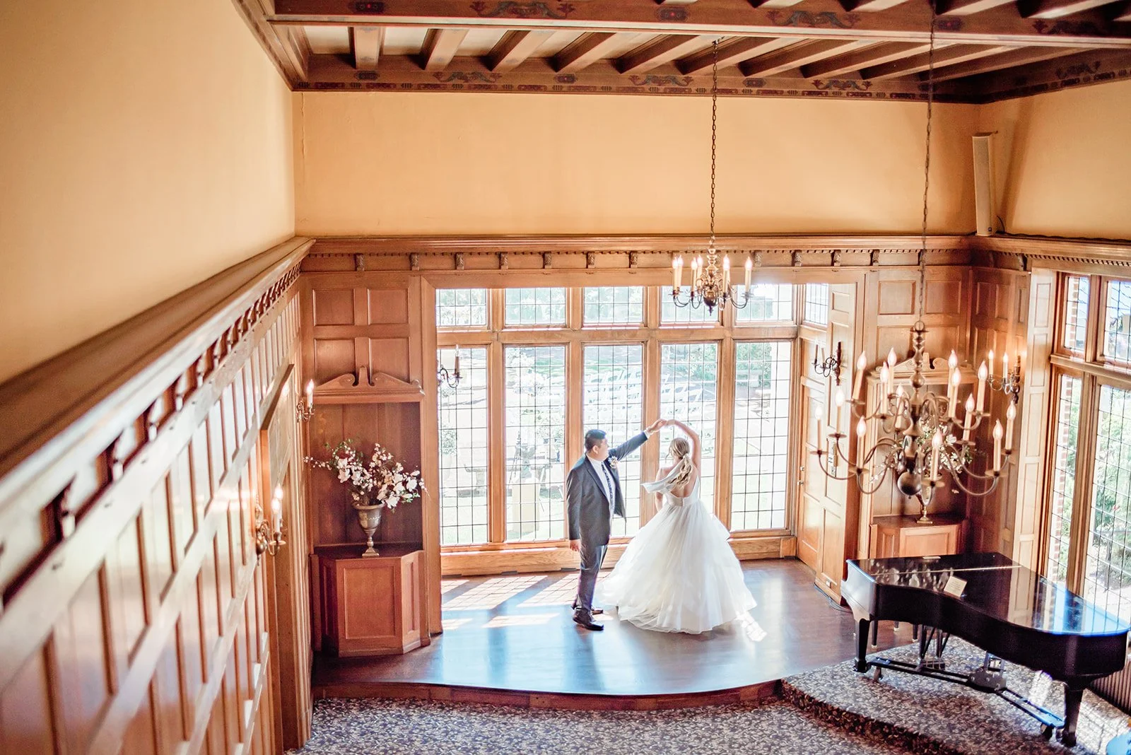 Bride and groom dancing on the ballroom stage at Lairmont Manor, backlit by floor-to-ceiling vintage leaded glass windows, with a grand piano to the right