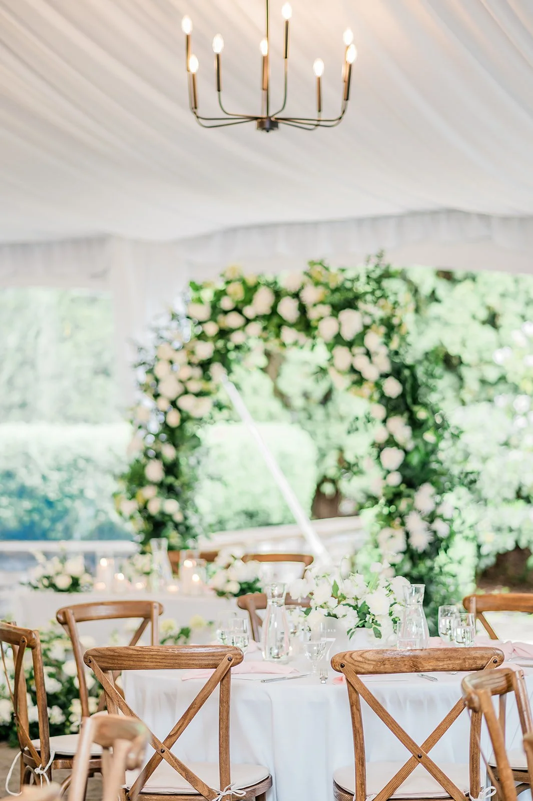 Reception tables set under the tent with the floral arch at Chateau Lill