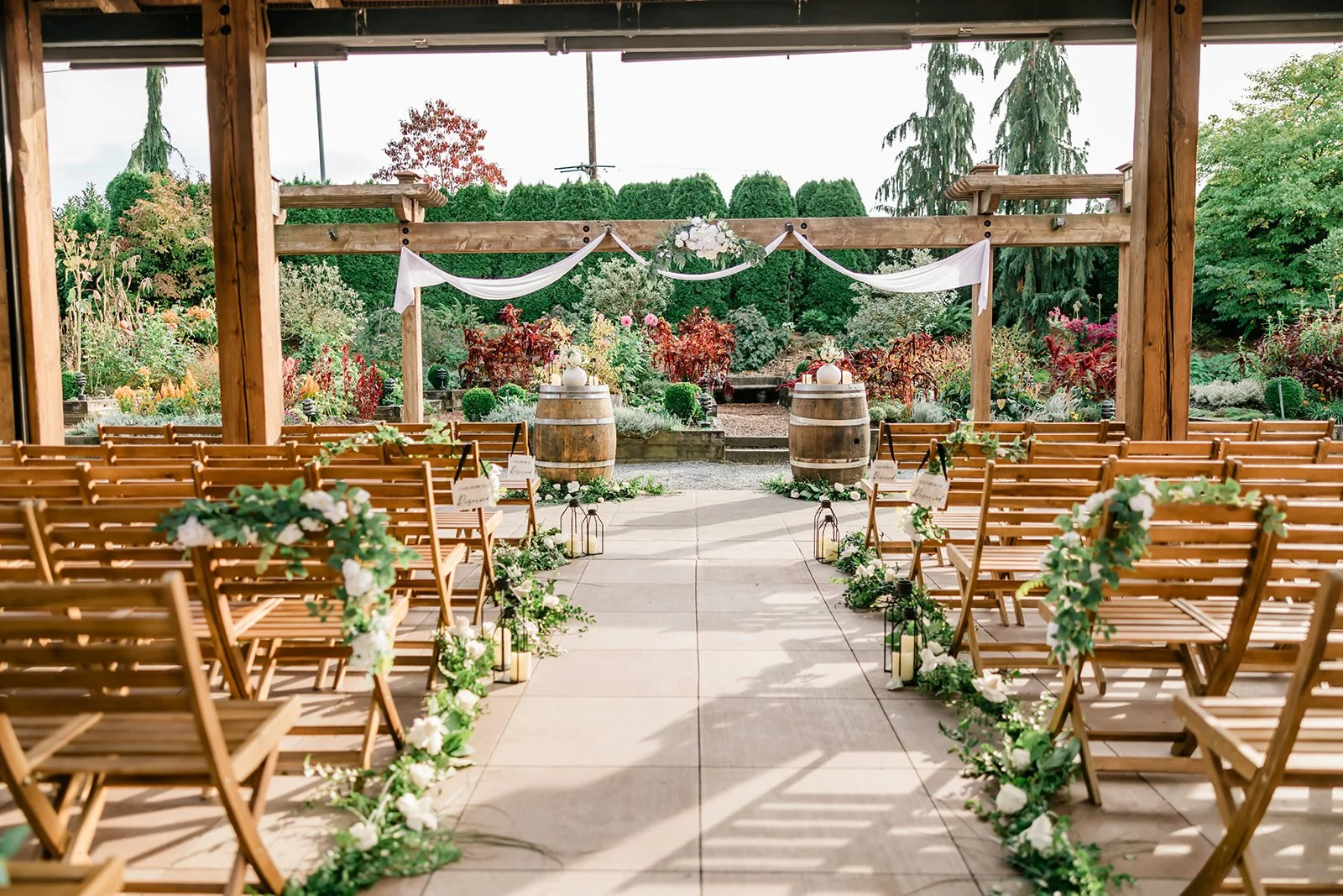 Empty ceremony aisle at Willows Lodge lined with wine barrels, white florals, and garden backdrop