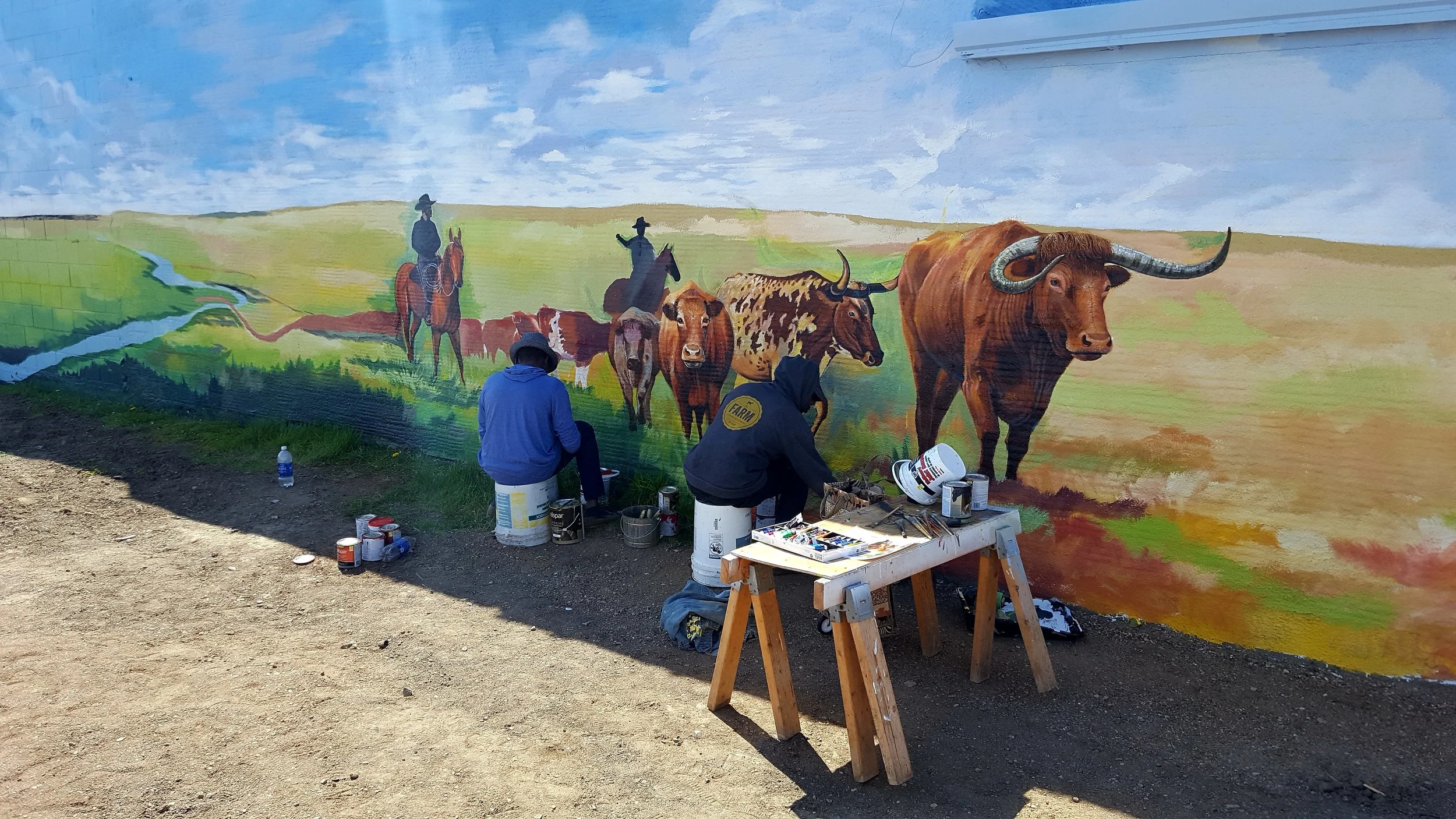 A mural in Boss Cowman Square in progress. This hand painted mural will be the back drop for the sculpture that I am doing for the square.