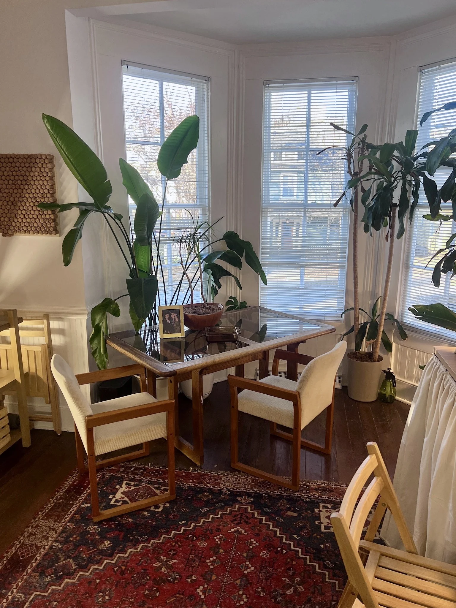 Cozy seating area inside the HEIR Raleigh studio with white armchairs, a glass table, large plants, and a red rug.
