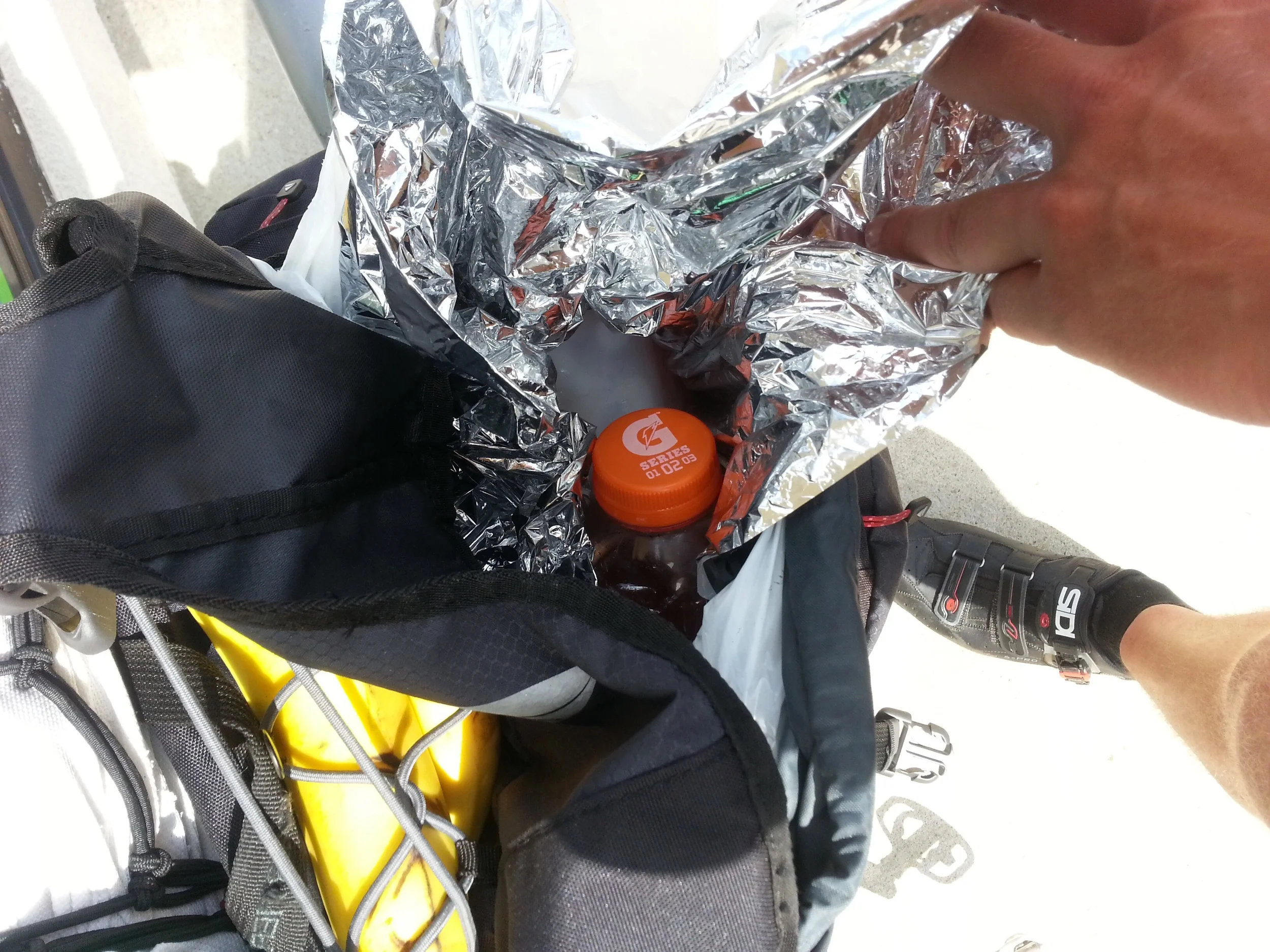 Experimental fridge - version 1: Garbage bag lined with an emergency blanket. A waterbottle filled with ice keeps all the other stuff cold. It worked for about 50kms and kept everything quite cold.